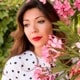 A woman with long brown hair and wearing white shirt and standing behind the oleander tree.