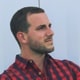 A man with short dark hair and wearing red and a navy blue checkered shirt.